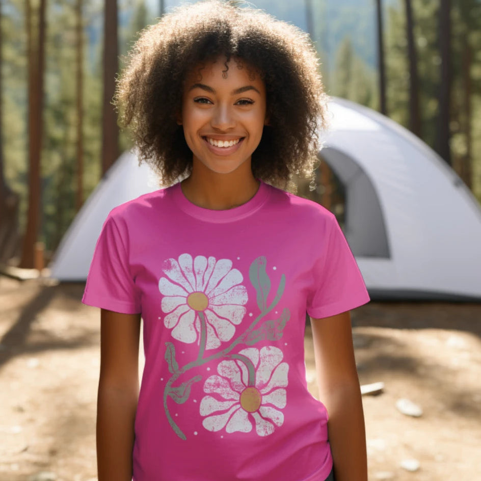 Person wearing a pink t-shirt with floral design in front of a tent in a forest setting
